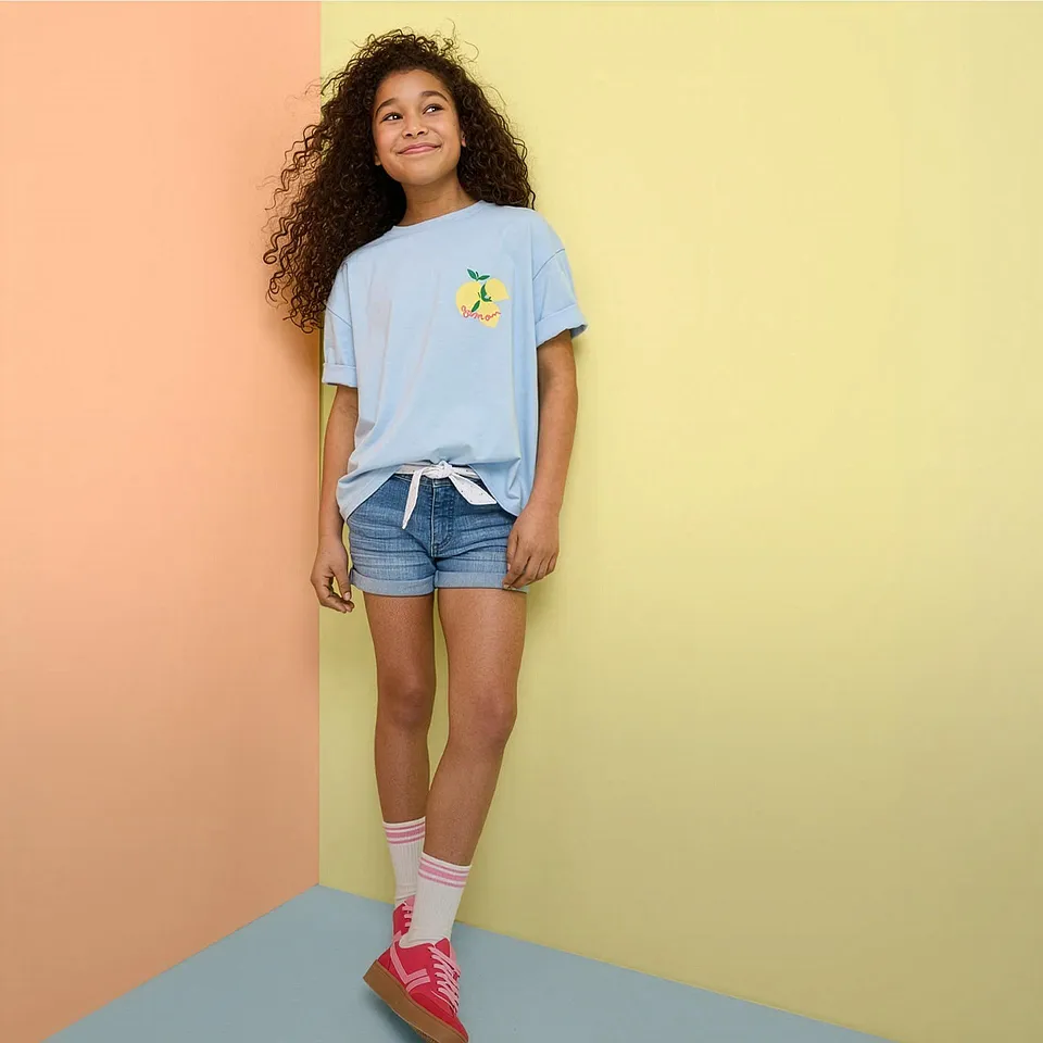 Sommerantrekk med lysebl&aring; T-skjorte, denimshorts og flerfargede sneakers.