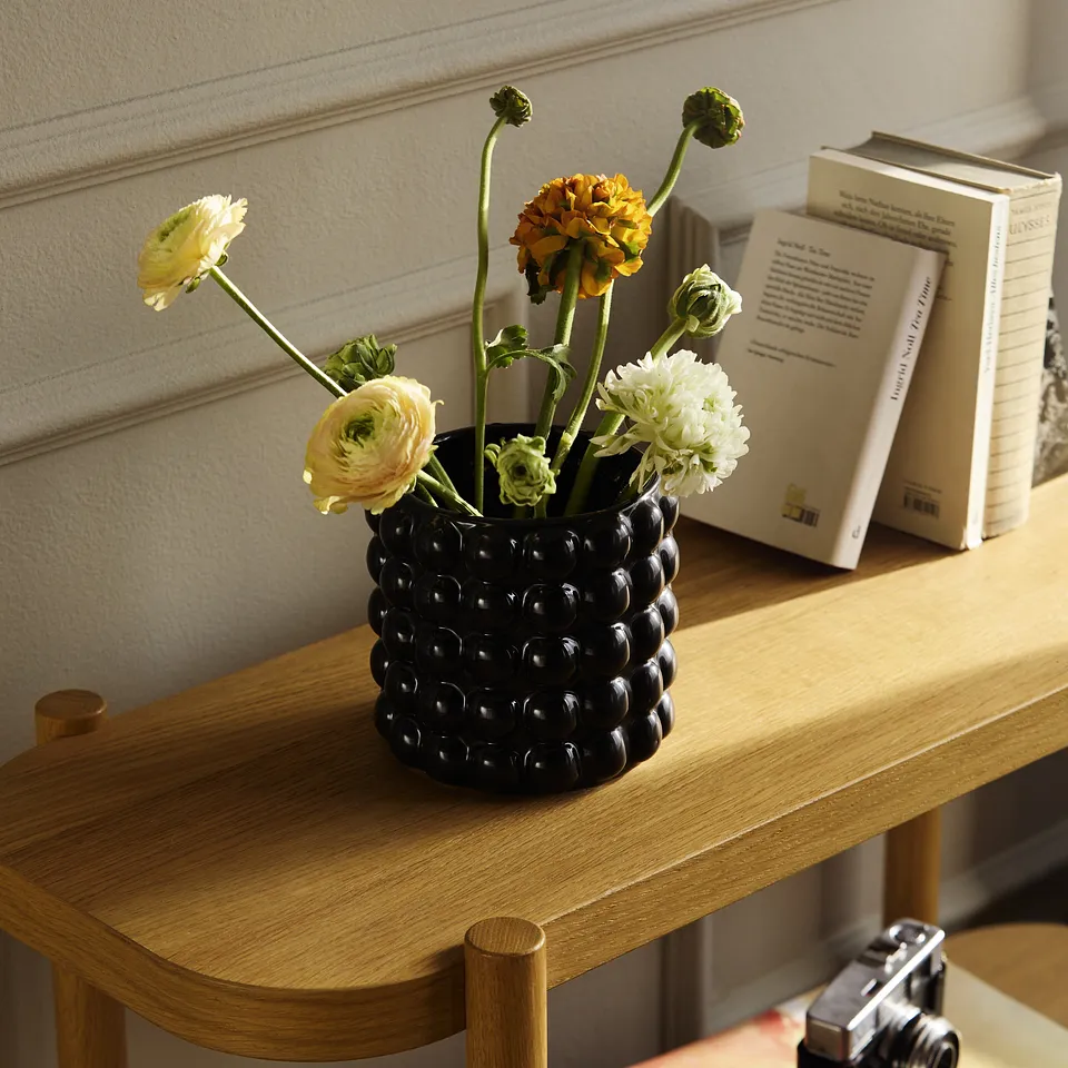 Sort vase med friske blomster og b&oslash;ker p&aring; et trebord.