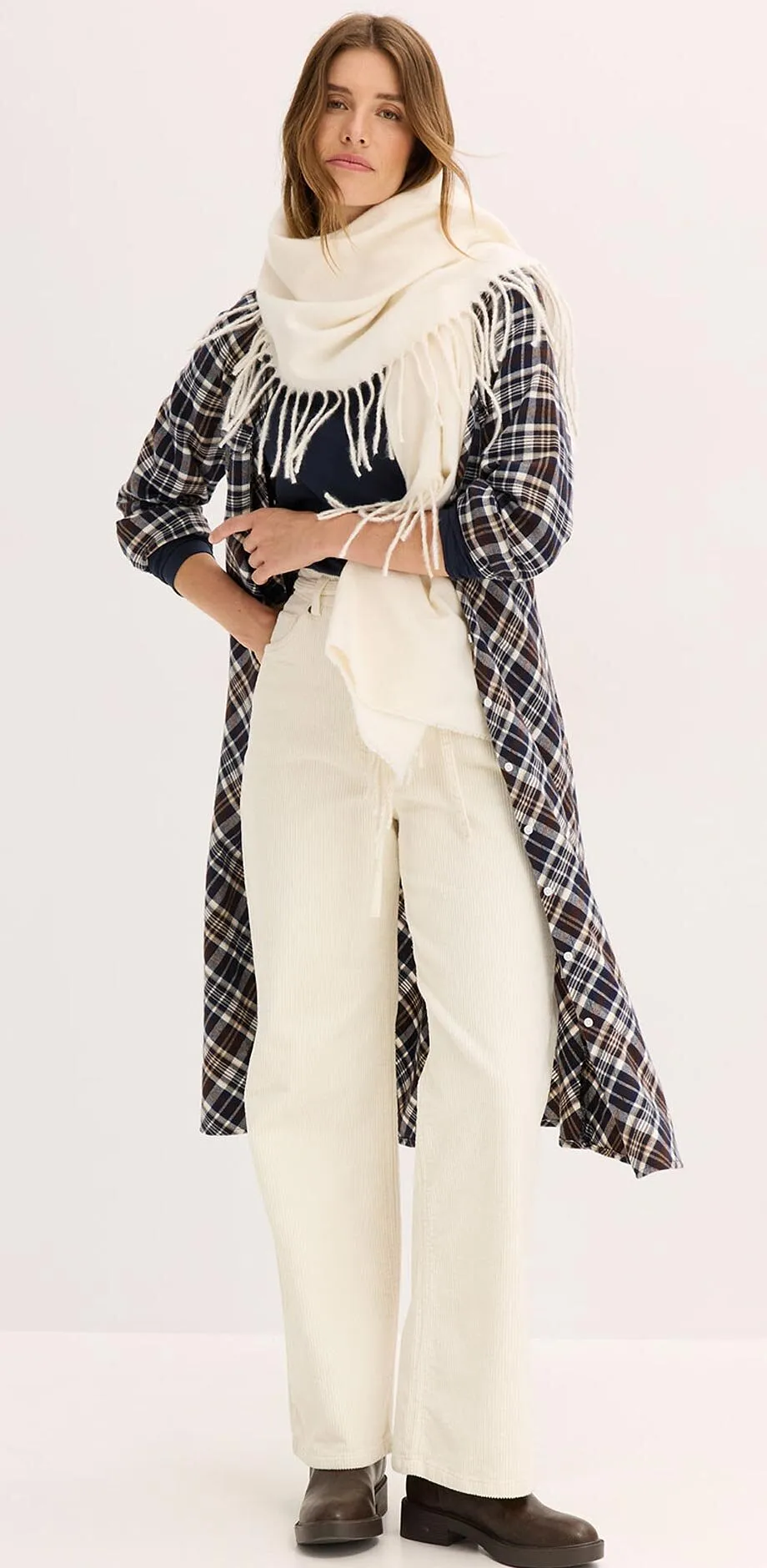 Rutete k&aring;pe over kremfarget antrekk best&aring;ende av h&oslash;yhalset genser, skjerf og bukse.