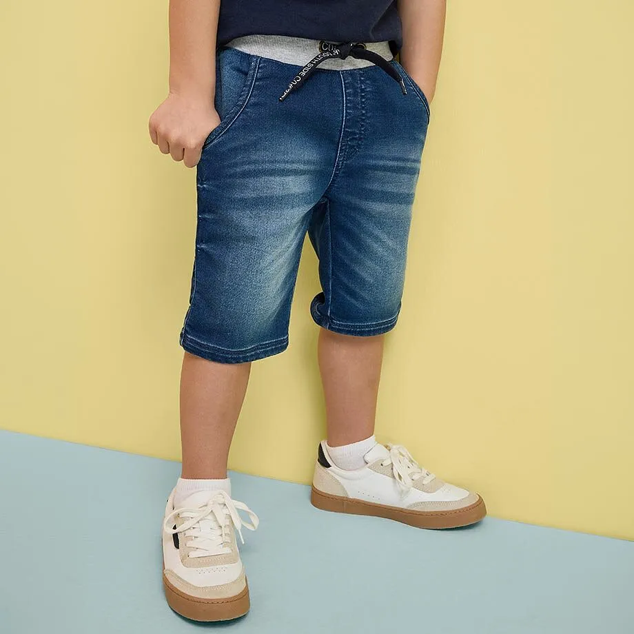 Barn i bl&aring; denimshorts og hvite sneakers.
