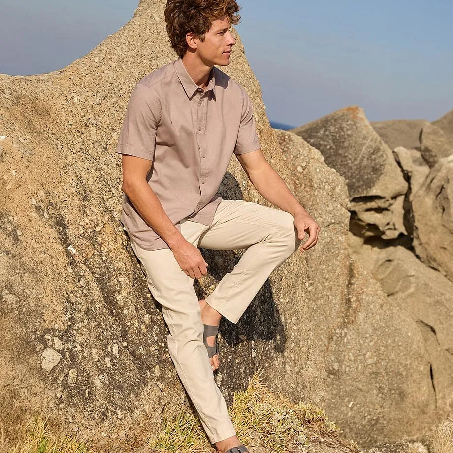 En man i beige skjorte og lyse chinos med sandaler p&aring; stranden.