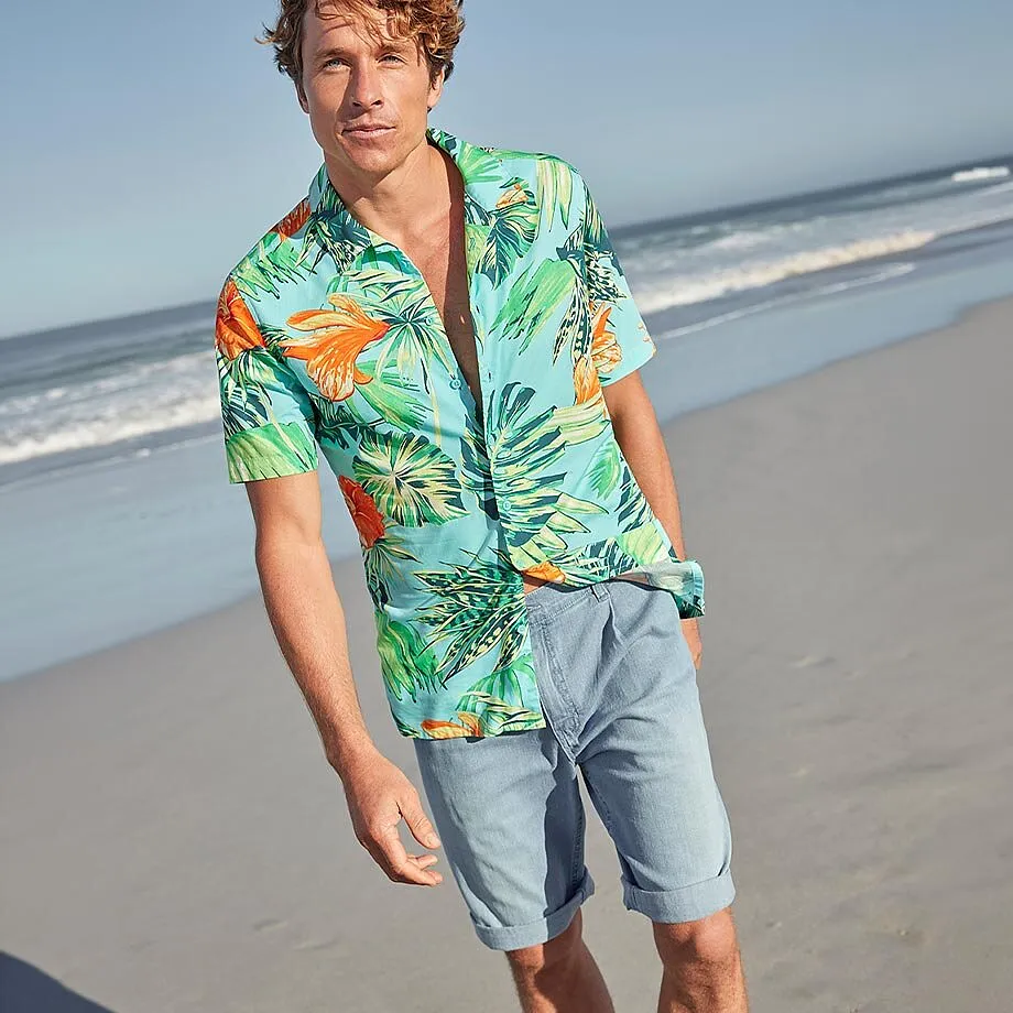 En mann i hawaiiskjorte og lys shorts p&aring; stranden.