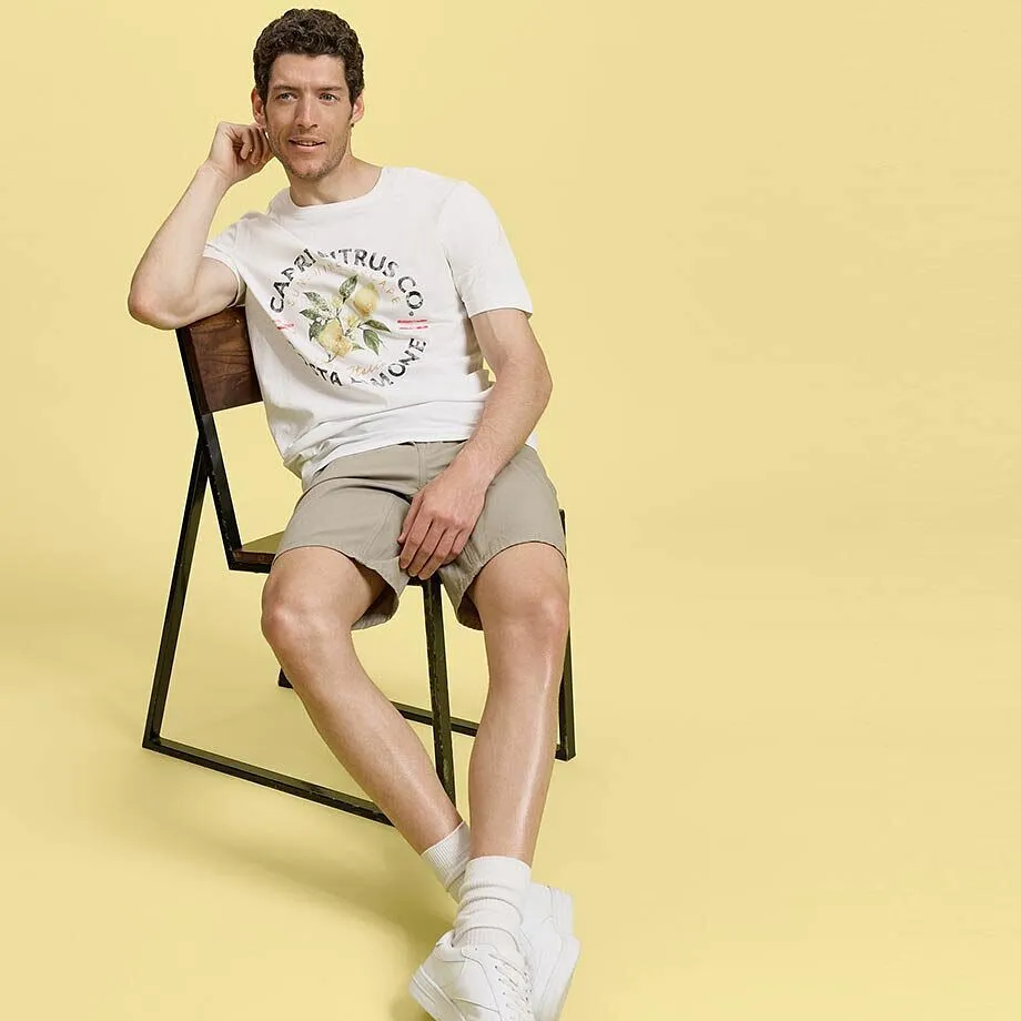 Et avslappet sommerantrekk: Hvit T-skjorte, beige shorts og hvite joggesko.