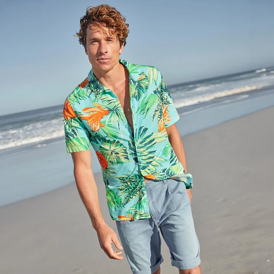 En mann i hawaiiskjorte og lys shorts p&aring; stranden.