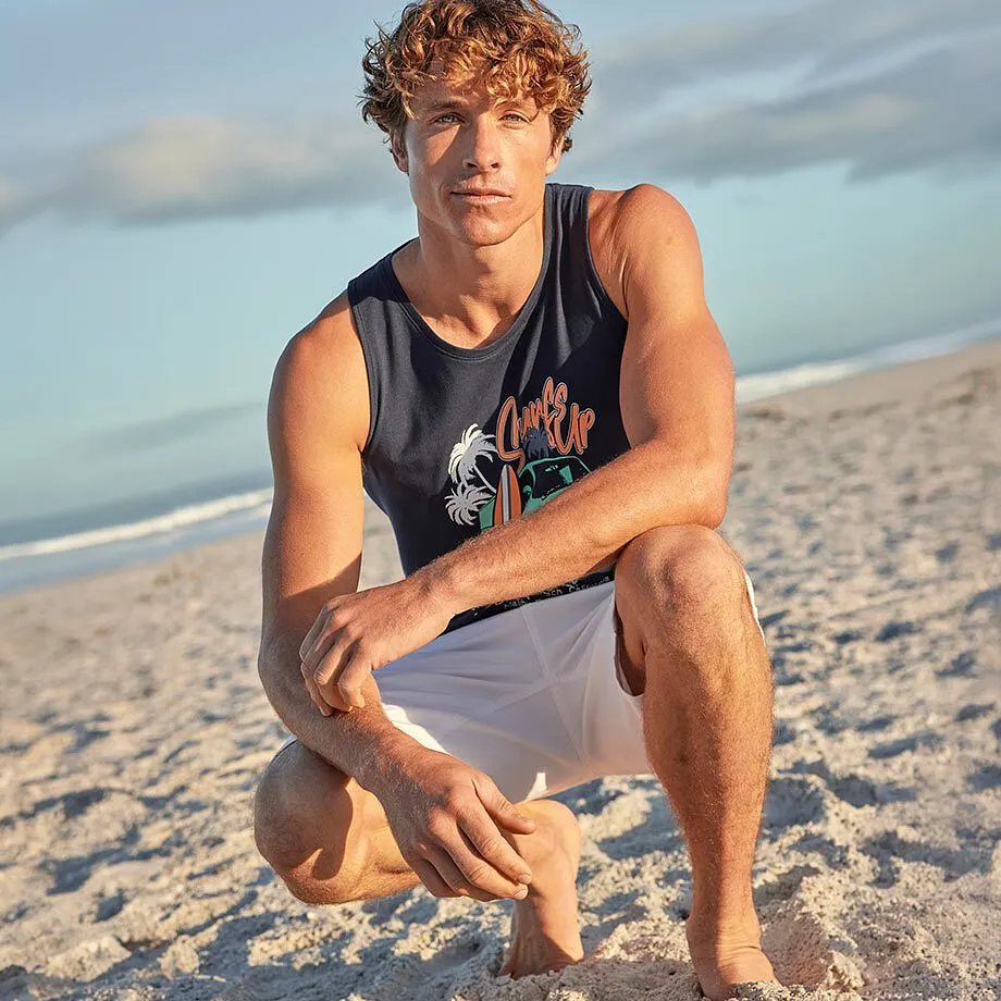 Person i bl&aring; singlet med trykk og hvit shorts p&aring; stranden.