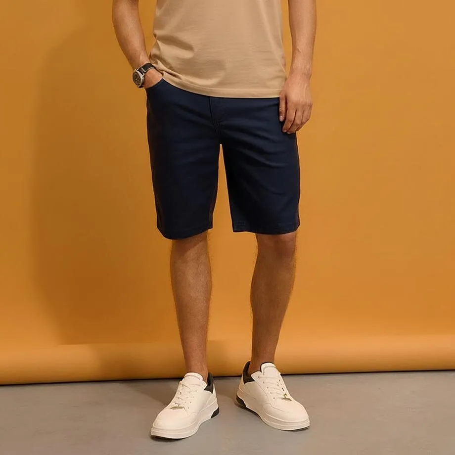 Beige T-skjorte, m&oslash;rkebl&aring; shorts og hvite sneakers.
