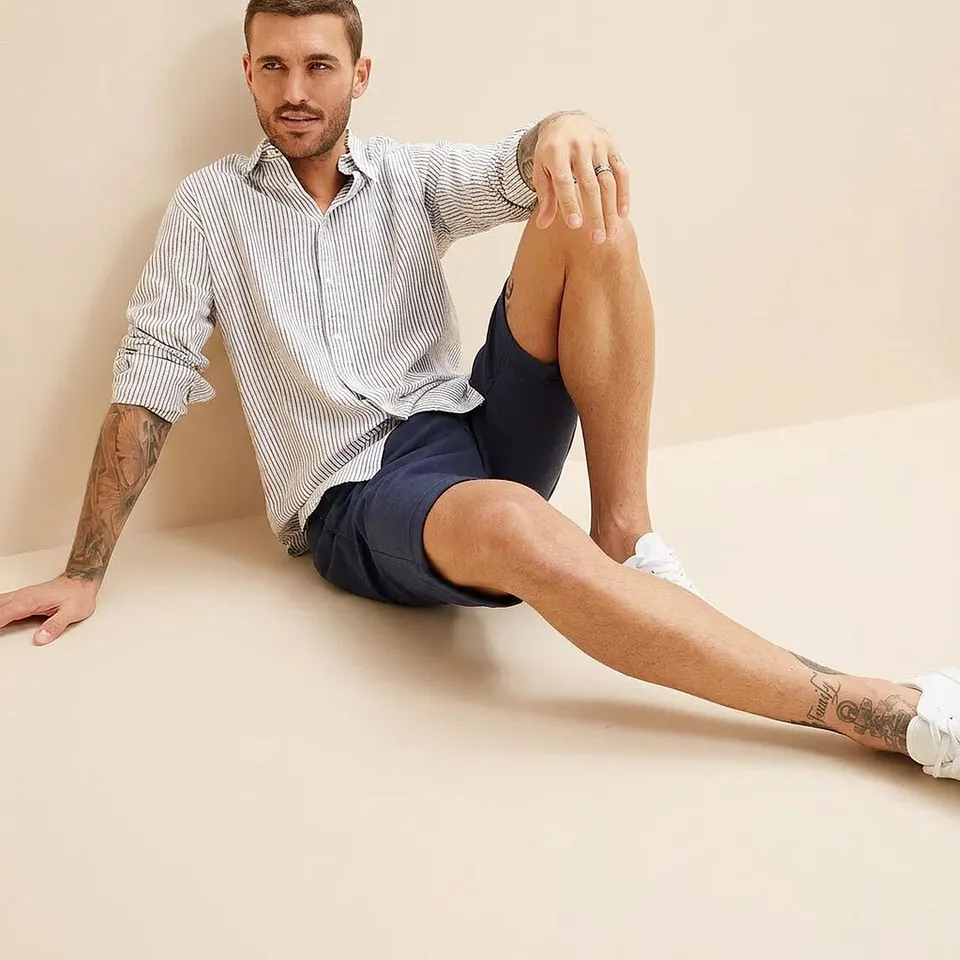 Person i stripete skjorte, m&oslash;rkebl&aring; shorts og hvite sneakers.