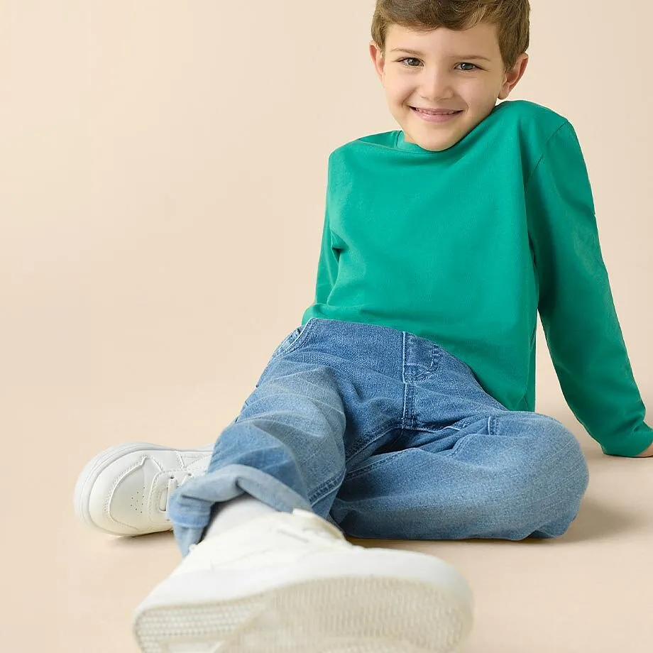 Gr&oslash;nn topp, bluejeans og hvite sneakers &ndash; behagelig antrekk til barn.