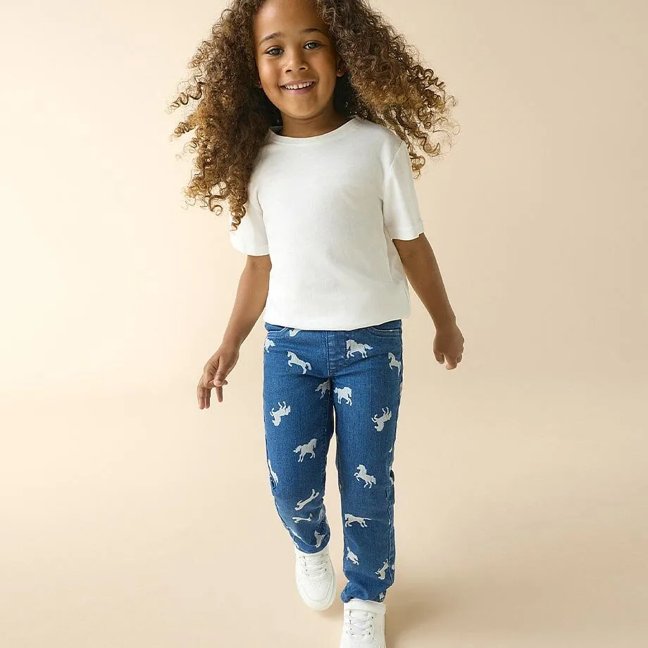 Barn i hvit T-skjorte, bluejeans med hestem&oslash;nster og hvite sneakers.