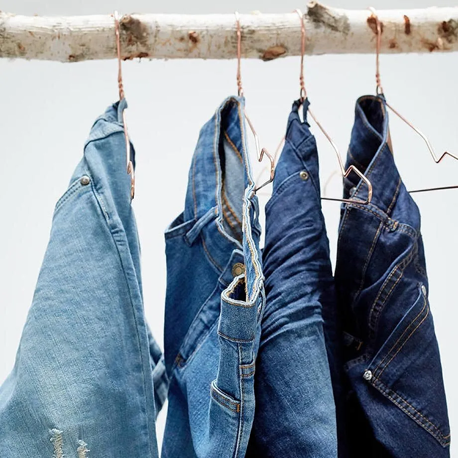 En rad bluejeans med ulik vasket effekt fint opphengte p&aring; kleshengere.