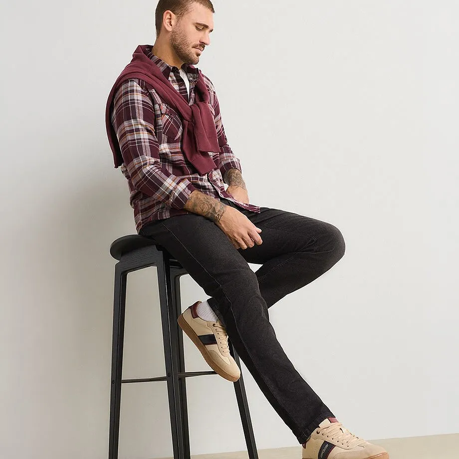 Hen i rutete skjorte, m&oslash;rke jeans, beige joggesko og vinr&oslash;d genser.