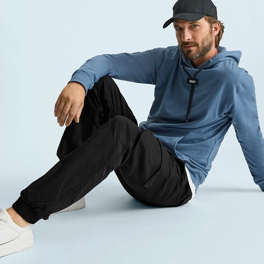 Hen i bl&aring; hettegenser, sort cargobukse, hvite sneakers og caps.