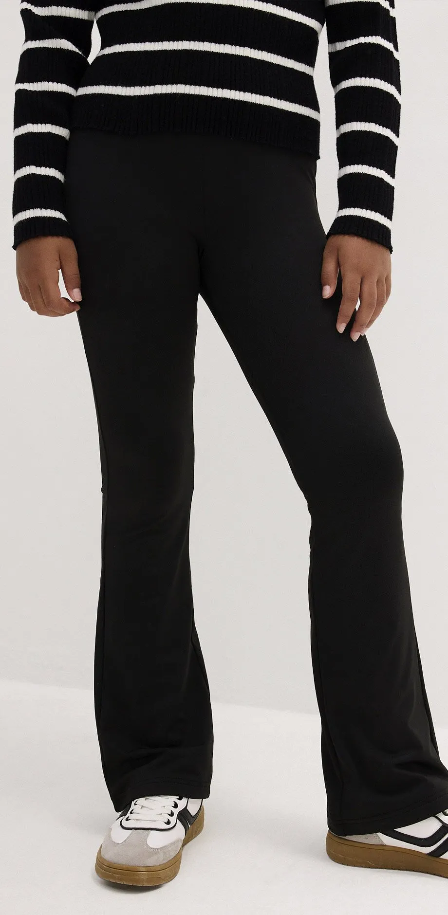Sort leggings med utsvingte ben, hvite og sorte sneakers og stripete genser.