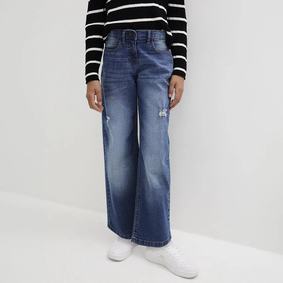 Barn i stripete, langermet topp, bl&aring;, utsvingte jeans og hvite sneakers.