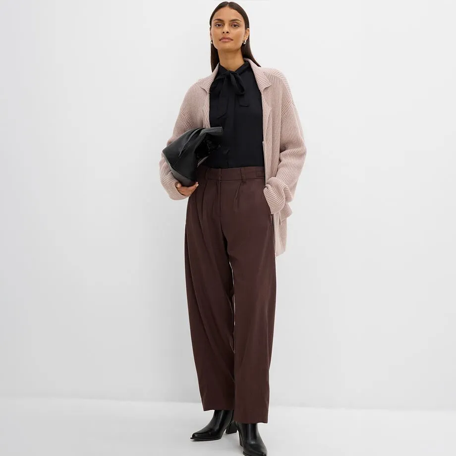 Hen i sort skjorte, beige cardigan, brun bukse og sorte ankelst&oslash;vletter.