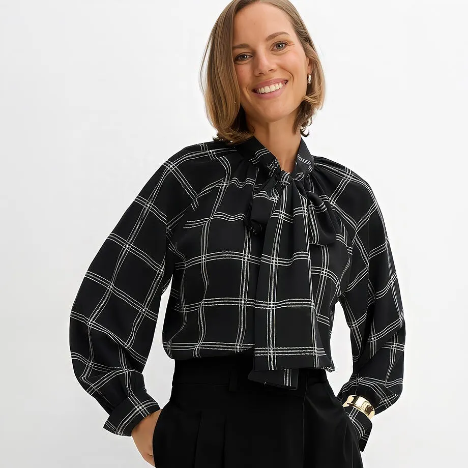 Elegant, sort knytebluse med rutem&oslash;nster, sort bukse og gullfarget armring.