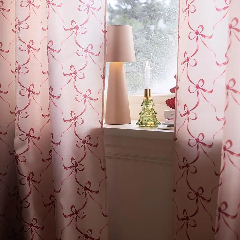 Vindu pyntet med rosa gardiner med sl&oslash;yfem&oslash;nster samt lampe og levende lys.