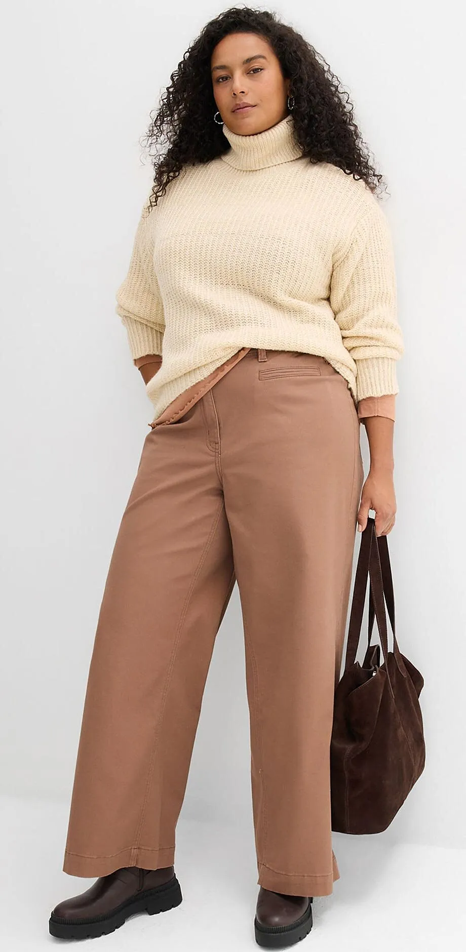 Kremfarget strikkegenser og brun bukse.